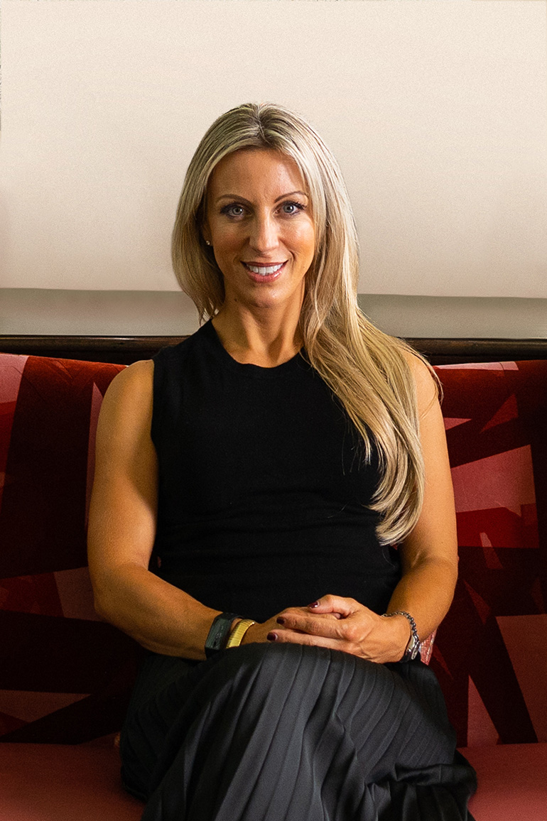 Jen Brockwell of Reframe Capital sits on a red chair smiling towards the camera